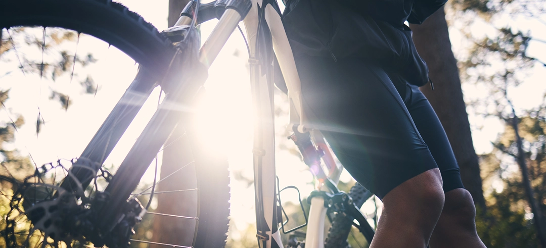 Persona apoyada en una bicicleta mientras una ruta con el sol de fondo