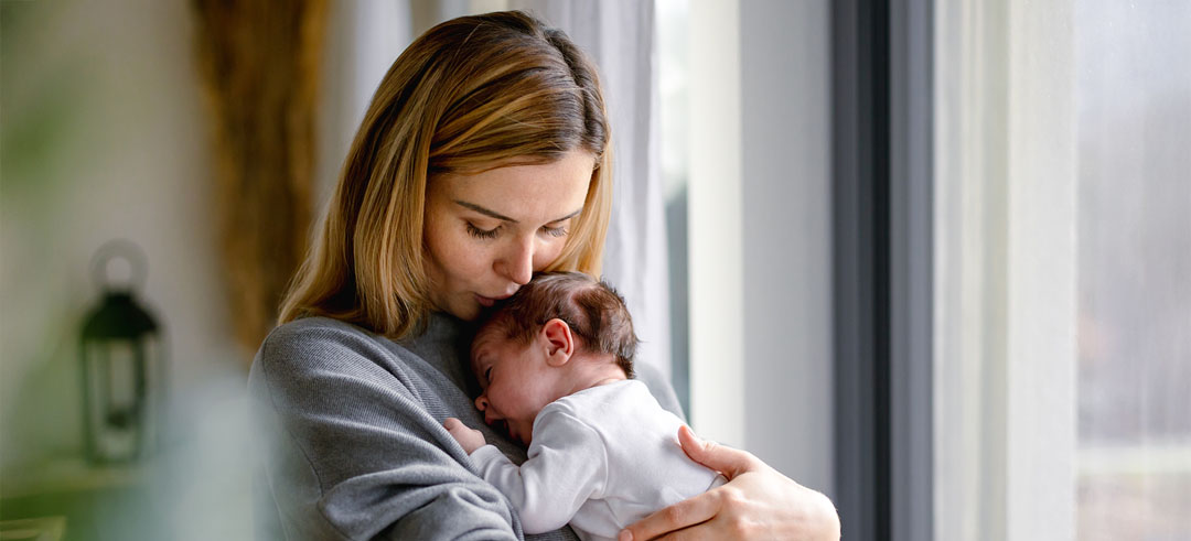 Mujer sosteniendo un bebé sobre sus brazos y apoyado en su pecho